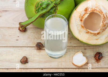 Frische Kokosnuss Wassertrinken aus Glas mit Kokos-Blatt auf hölzernen Hintergrund Stockfoto
