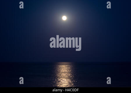 Vollmond in einer klaren Nacht draußen am Horizont über dem Meer Stockfoto