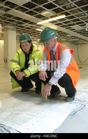 Männliche und weibliche Bauarbeiter untersuchen eine Konstruktionszeichnung in einem teilweise komplette Bürogebäude in central London, UK Stockfoto