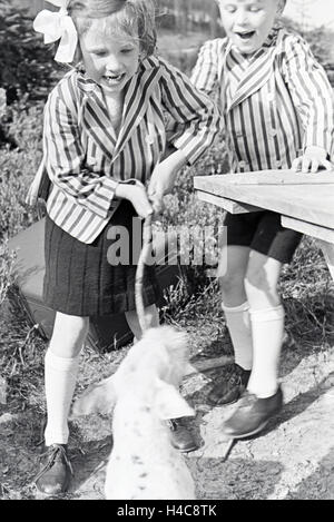 Zwei Kinder in Gestreiften Jacketts Beim Spielen Mit Einem Hund, Deutschland, 1930er Jahre. Zwei Kinder in gestreiften Jacken spielen mit einem Hund, Deutschland, 1930er Jahre Stockfoto