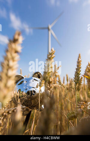 Sparschwein in ein Getreidefeld, im Hintergrund ein Windkraftwerk Stockfoto