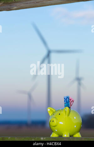 Sparschwein im Abendlicht im Hintergrund ein Windkraftwerk Stockfoto