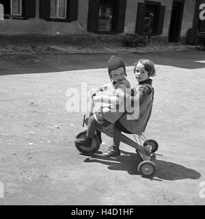 Zwei Kinder Spielen Mit Einem Dreirad, 1930er Jahre Deutschland. Zwei Kinder spielen mit einem Dreirad, Deutschland der 1930er Jahre. Stockfoto