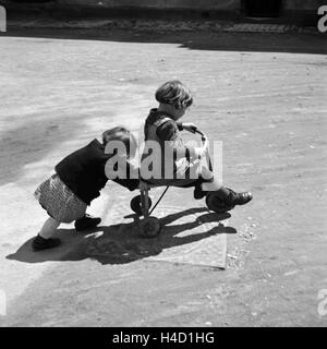 Zwei Kinder Spielen Mit Einem Dreirad, 1930er Jahre Deutschland. Zwei Kinder spielen mit einem Dreirad, Deutschland der 1930er Jahre. Stockfoto