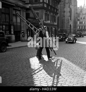 Zwei Maler Oder Fensterputzer Auf der Straße Vor der Buchhandlung Lindemann in Stuttgart, Deutschland, 1930er Jahre. Zwei Maler oder Fensterreiniger überqueren der Straße vor Lindemanns Buch bei Stuttgart, Deutschland der 1930er Jahre lagern. Stockfoto