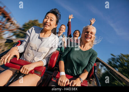 Junge Menschen auf eine rasante Achterbahn-Fahrt. Gruppe von Freunden, die Spaß im Freizeitpark. Stockfoto