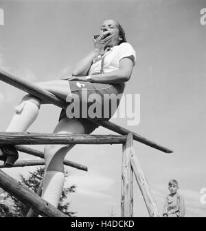 Eine Junge Frau Mit Einer Mundharmonika Auf Einem Zaun, 1930er Jahre Deutschland. Eine junge Frau mit einer Mundharmonika auf einem Zaun, Deutschland der 1930er Jahre. Stockfoto