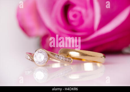 Ringe aus Gold auf einer weißen Fläche mit einer Rose im Hintergrund. Stockfoto