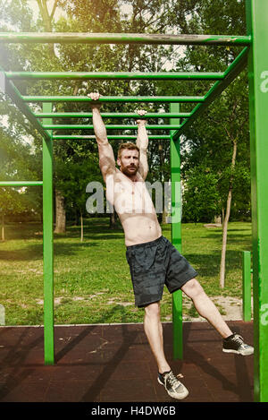 Junger Mann Zug tut ups auf horizontalen Balken im Freien Stockfoto