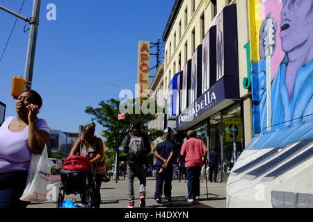 Fußgänger an der 125th Street mit dem Zeichen des Apollo Theater im Hintergrund. Harlem, New York City, USA Stockfoto