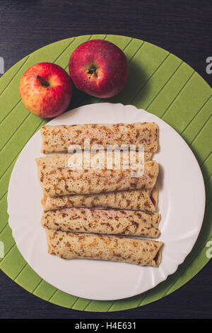 Geröstete gerollte Pfannkuchen auf einem weißen runden Platte und zwei Äpfel in der Nähe. Ansicht von oben. Flach zu legen Stockfoto