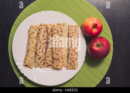 Geröstete gerollte Pfannkuchen auf einem weißen runden Platte und zwei Äpfel in der Nähe. Ansicht von oben. Flach zu legen Stockfoto