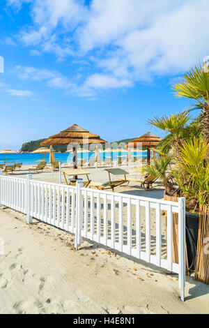 Liegestühle und Sonnenschirme mit weißen Holzzaun am Strand von Porto Giunco, Insel Sardinien, Italien Stockfoto