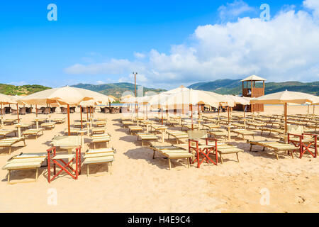 Liegestühle mit Sonnenschirmen auf Sand und Blick auf türkisfarbenes Meerwasser, Sa Colonia, Insel Sardinien, Italien Stockfoto