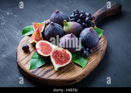 Obst-Teller: frische Feigen und schwarzen Trauben 'Isabella' auf Holzbrett. Horizontale Stockfoto