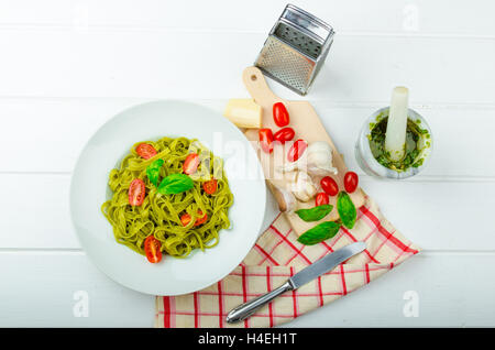 Spinat-Tagliatelle mit Basilikum-Pesto und Mini-Tomaten, Holzplatte, Servietten und Pesto Mörser Stockfoto