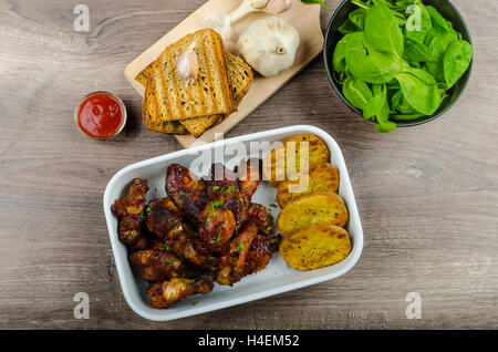 Klebrige Hähnchenflügel mit Knoblauch Brot Panini, rustikal würzige Kartoffeln, frische Spinatblätter Stockfoto