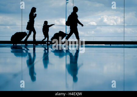 Silhouette der jungen Familie mit Gepäck zu Fuß am Flughafen, Mädchen am Fenster zeigen Stockfoto