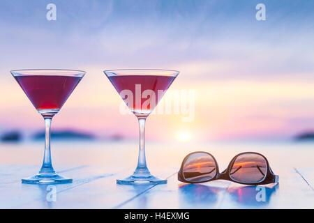 Zwei Cocktails und Sonnenbrillen auf einem Tisch von luxuriösen tropischen Strand Resort Restaurant mit wunderschönen Sonnenuntergang im Hintergrund Stockfoto