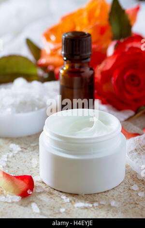 Gesichtscreme mit Rosen, Flasche Aromatherapie ätherische Öl und Salz auf braunen Stein Hintergrund. Rose Spa. Stockfoto