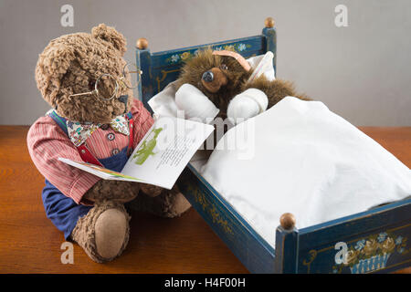 Krank Teddybär mit bandagierten Pfoten und Kopf, mit Thermometer, in ein original Pumuckl Kinderbett, großer Teddybär mit Brille und Stockfoto