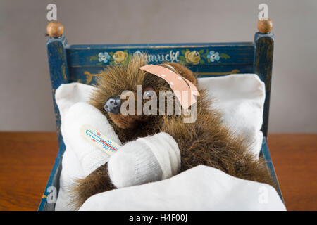 Kranke Teddy bandagiert Pfoten und Kopf, mit Thermometer, in ein original Pumuckl-Krippe Stockfoto