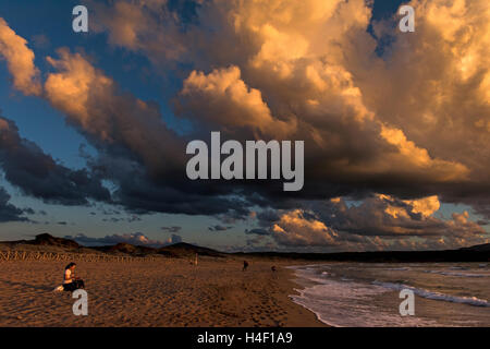 Junge Frau sitzt am Strand bei Sonnenuntergang, Porto Ferro, Sardinien, Italien Stockfoto