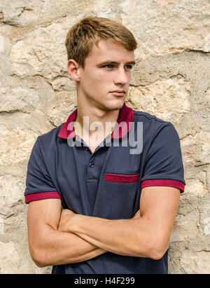 Hübscher junger Mann lehnte sich gegen die Mauer aus Stein, die mit verschränkten Armen. Stockfoto