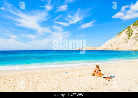 Nicht identifizierte junge attraktive Frau sitzen auf Sandstrand und azurblaues Meer mit Meerblick im Petani Bucht, Insel Kefalonia, Griechenland Stockfoto