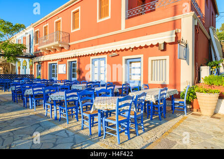 Blaue Stühle und Tische vor traditionelle griechische Taverne in Fiskardo Hafen, Insel Kefalonia, Griechenland Stockfoto