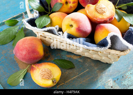 Ernten Sie frische reife Pfirsiche in einem Weidenkorb auf dem Vintage Holztisch, selektiven Fokus. Stockfoto