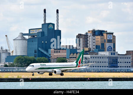 Flugzeug Alitalia Embraer rollen, bevor Sie zum Flughafen London City Tate & Lyle Silvertown Zuckerfabrik Fabrikgebäude über Newham England Großbritannien Stockfoto