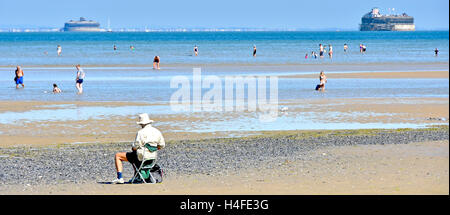 Rückseitige Ansicht älterer Mann sitzt allein auf der Isle Of Wight UK Urlaub Strand bei Ebbe skizzieren einen Blick auf den Solent, einschließlich zwei Forts an heißen Sommertag Stockfoto