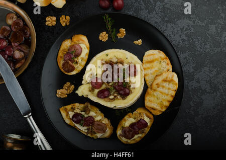 Brie Käse gebacken mit Nüssen und Trauben, leckere und knusprige Baguette und Bio-Kräuter, Reduzierung von Zucker, Nüssen und Balsamico-Essig Stockfoto