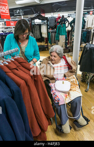 Eine ältere Dame im Rollstuhl Geschäfte für eine neue Jacke in einem Kaufhaus mit Ihrem Betreuer oder Helfer. Stockfoto
