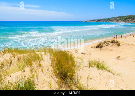 Rasen Sie auf Sanddüne bei Chia Strand und junge Frau, die in der Ferne gegen einen Zaun, Insel Sardinien, Italien Stockfoto