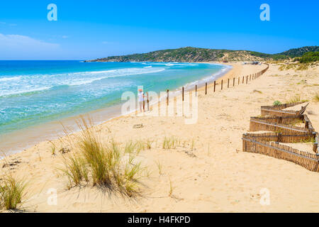 Rasen Sie auf Sanddüne bei Chia Strand und junge Frau, die in der Ferne gegen einen Zaun, Insel Sardinien, Italien Stockfoto