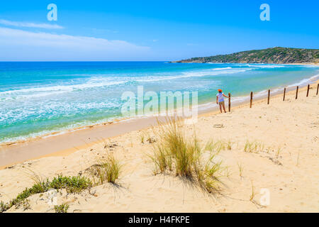 Rasen Sie auf Sanddüne bei Chia Strand und junge Frau, die in der Ferne gegen einen Zaun, Insel Sardinien, Italien Stockfoto