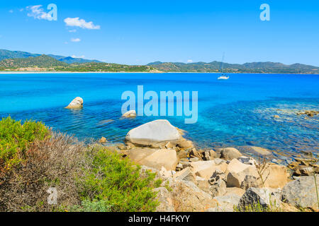 Felsen im wunderschönen türkisfarbenen Meerwasser auf Küste von Porto Giunco Bucht mit Yacht Boot im Hintergrund, Insel Sardinien, Italien Stockfoto