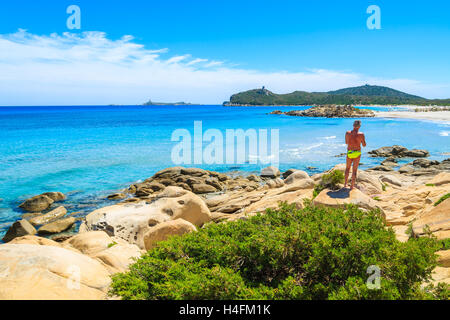 PORTO GIUNCO BAY, Insel Sardinien - 27. Mai 2014: Mann Touristen auf einem Felsen Blick auf türkisfarbenes Meerwasser auf Insel Sardiniens Villasimius-Halbinsel, Italien. Stockfoto