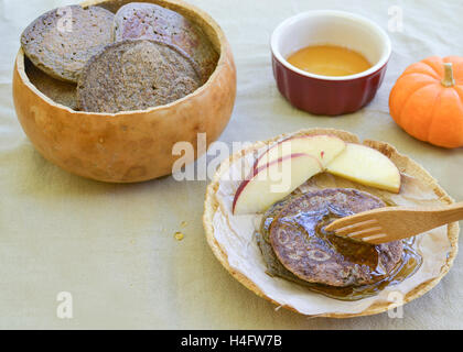 Rustikale Mahlzeit von Buchweizen Pfannkuchen Teller und Schale aus Kürbissen auf Blume Sac Tischdecke, begleitet von Ahornsirup Stockfoto