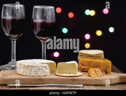 Brie und Hot Pepper jack Käse auf Holzbrett mit Crackern und zwei Gläser Rotwein, vor schwarzem Hintergrund Stockfoto