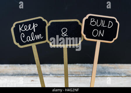 Halten Sie Ruhe und bauen auf Nachricht mit Kreide auf die Tafel Mini-Etiketten, defokussierten Tafel und Holztisch im Hintergrund geschrieben. Spaß und Humor-Konzept Stockfoto