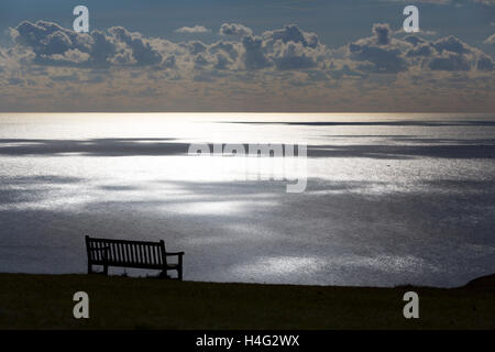 leeren Park Sitzbank auf Tennyson Down mit Blick auf Meer, Sonne und Wolken reflektiert von der Oberfläche Stockfoto