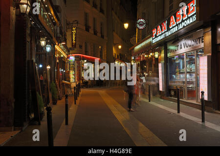 PARIS, Frankreich 13. August 2016: ein Blick auf eine Straße in Paris bei Nacht zeigt die Bewegungsunschärfe von Menschen und Restaurants, Cafés und andere Geschäfte Stockfoto