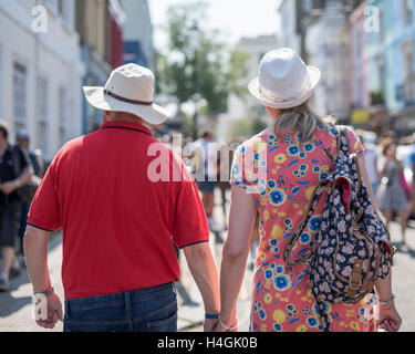 Ein paar tragen Sonnenhüte, die durch eine Straße hand in hand gehen Stockfoto