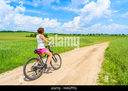 Junge attraktive Frau, die mit dem Fahrrad auf der Landstraße in grüne Sommerlandschaft, Polen Stockfoto