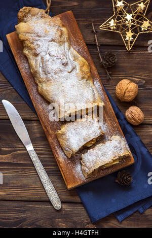 Weihnachten selbstgemachter Kuchen. Apfelstrudel (Pie) mit Rosinen, Walnüssen und Puderzucker mit Weihnachts-Dekor hautnah. Stockfoto