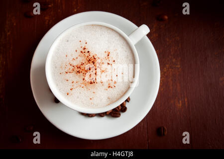 Tasse Cappuccino Kaffee mit Kakao Topping über rustikale Holz dunkel Stockfoto