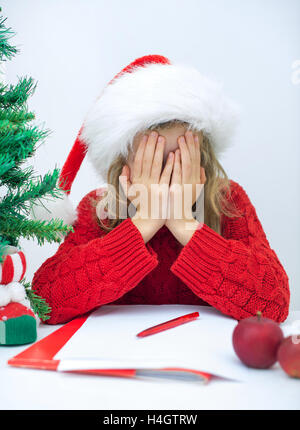 Traurige Mädchen im roten Hut einen Brief an den Weihnachtsmann schreiben. Stockfoto